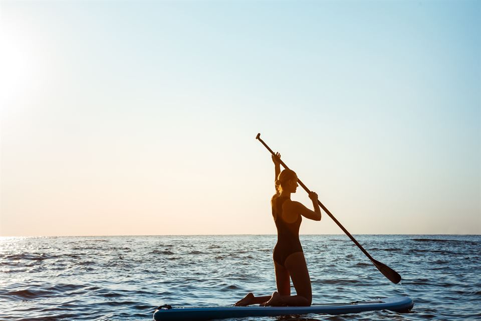 Silhouette of young beautiful girl surfing in sea at sunrise. Outdoors.
